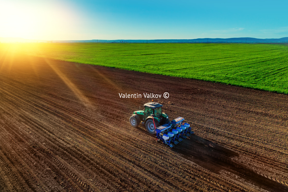 "Farmer with tractor seeding crops at field" stock image