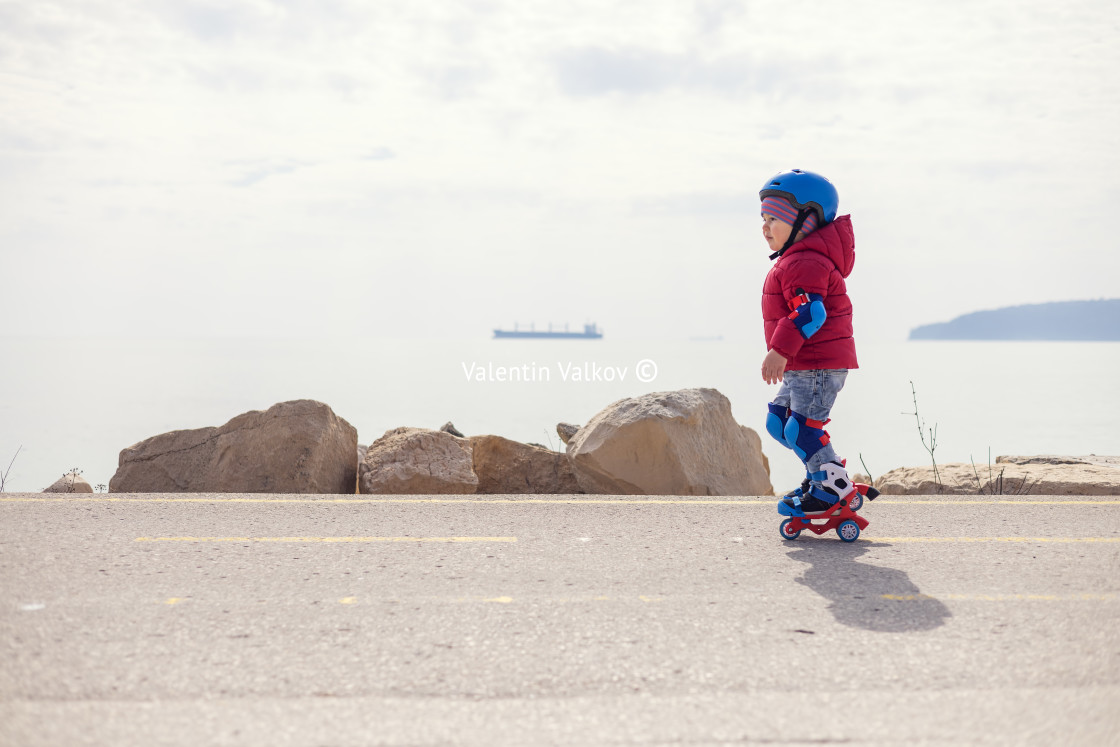 "Little baby boy riding roller skates near seashore. Kid with hel" stock image