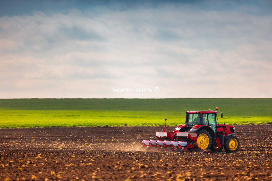 "Farmer with tractor seeding crops at field" stock image