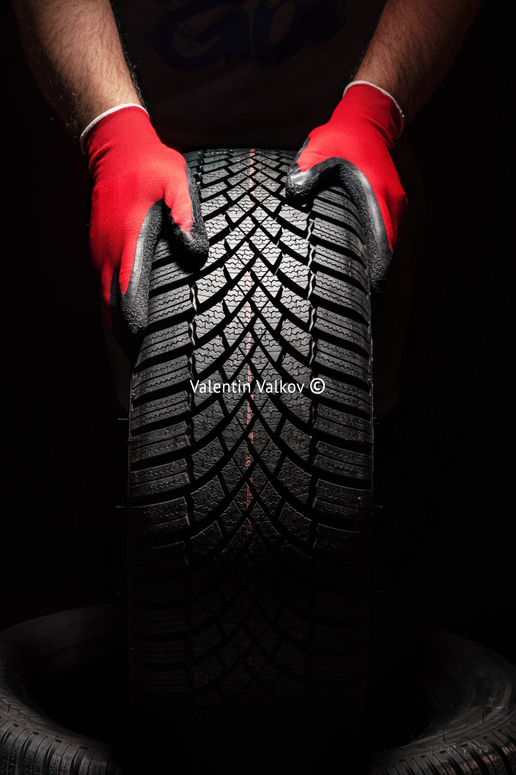 "Car tire service and hands of mechanic holding new tyre on black" stock image