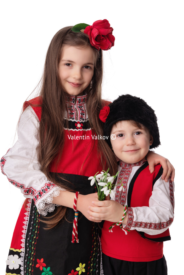 "Bulgarian kids boy and girl in traditional folklore costumes with spring flowers snowdrop and handcraft wool bracelet martenitsa symbol of Baba Marta" stock image