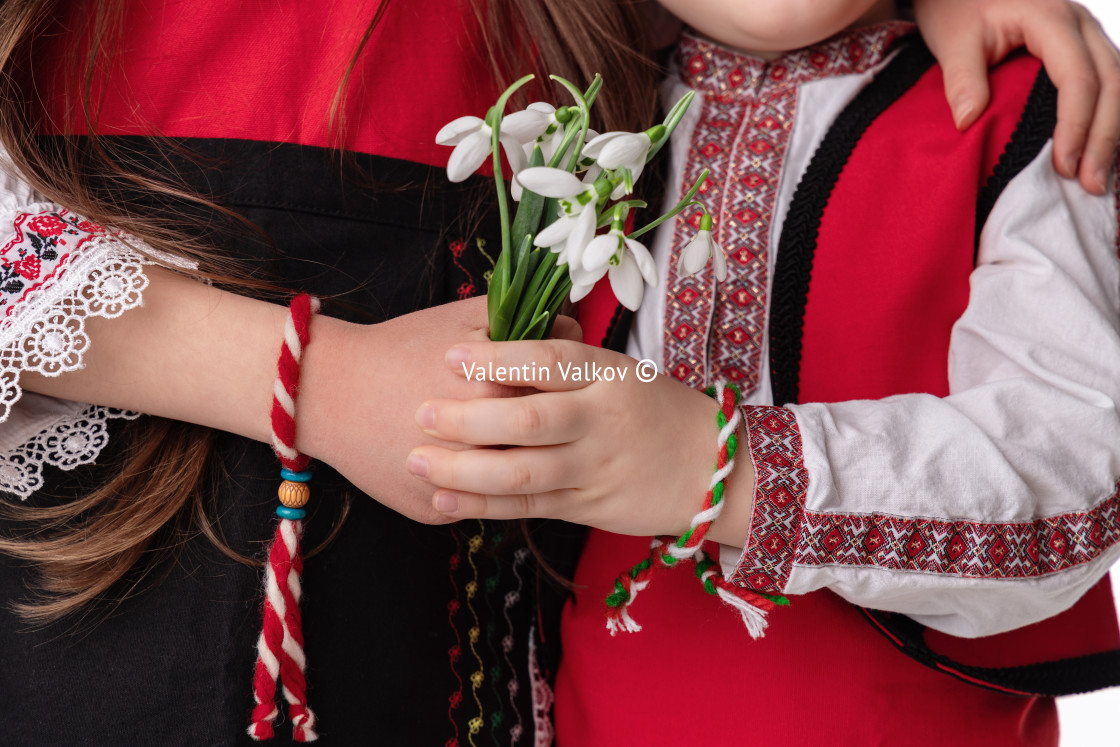 "Bulgarian kids boy and girl in traditional folklore costumes with spring flowers snowdrop and handcraft wool bracelet martenitsa symbol of Baba Marta" stock image