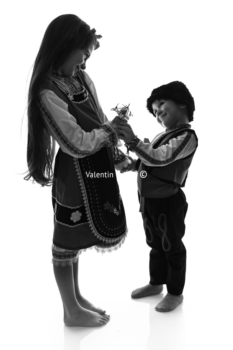 "Bulgarian kids boy and girl in traditional folklore costumes with spring flowers snowdrop and handcraft wool bracelet martenitsa symbol of Baba Marta" stock image