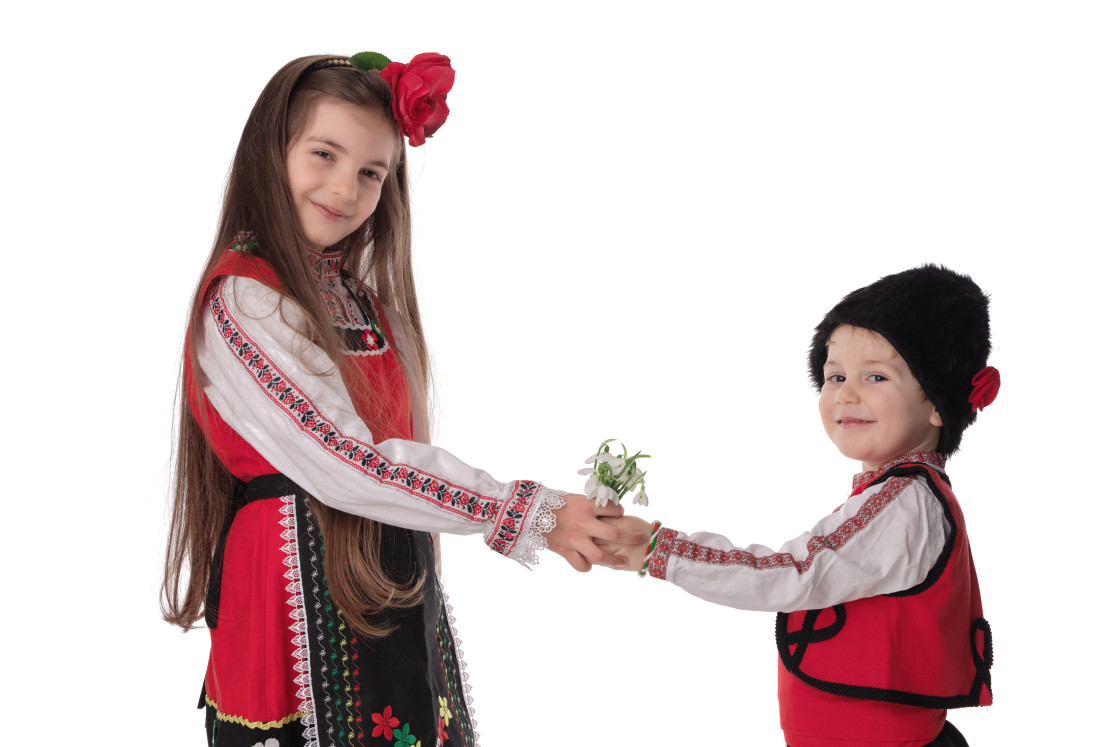 "Bulgarian kids boy and girl in traditional folklore costumes with spring flowers snowdrop and handcraft wool bracelet martenitsa symbol of Baba Marta" stock image