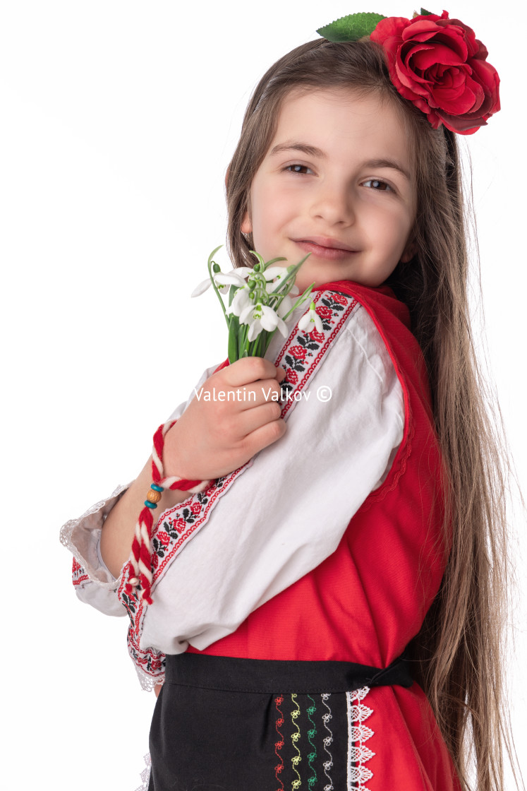 "Bulgarian girl in traditional folklore costumes with spring flowers snowdrop and handcraft wool bracelet martenitsa symbol of Baba Marta" stock image