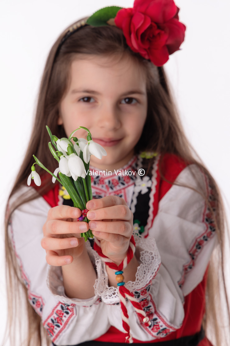 "Bulgarian girl in traditional folklore costumes with spring flowers snowdrop and handcraft wool bracelet martenitsa symbol of Baba Marta" stock image