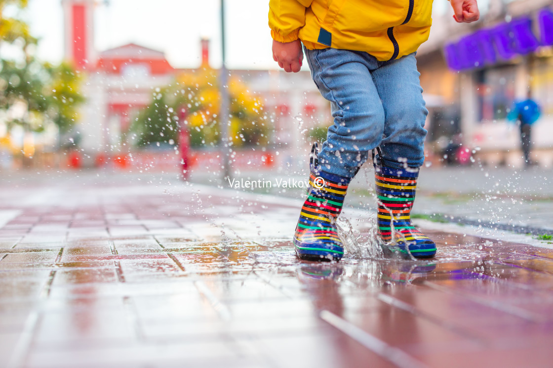 "Happy little kid boy jumping on rainy puddle in city street, autumn season" stock image