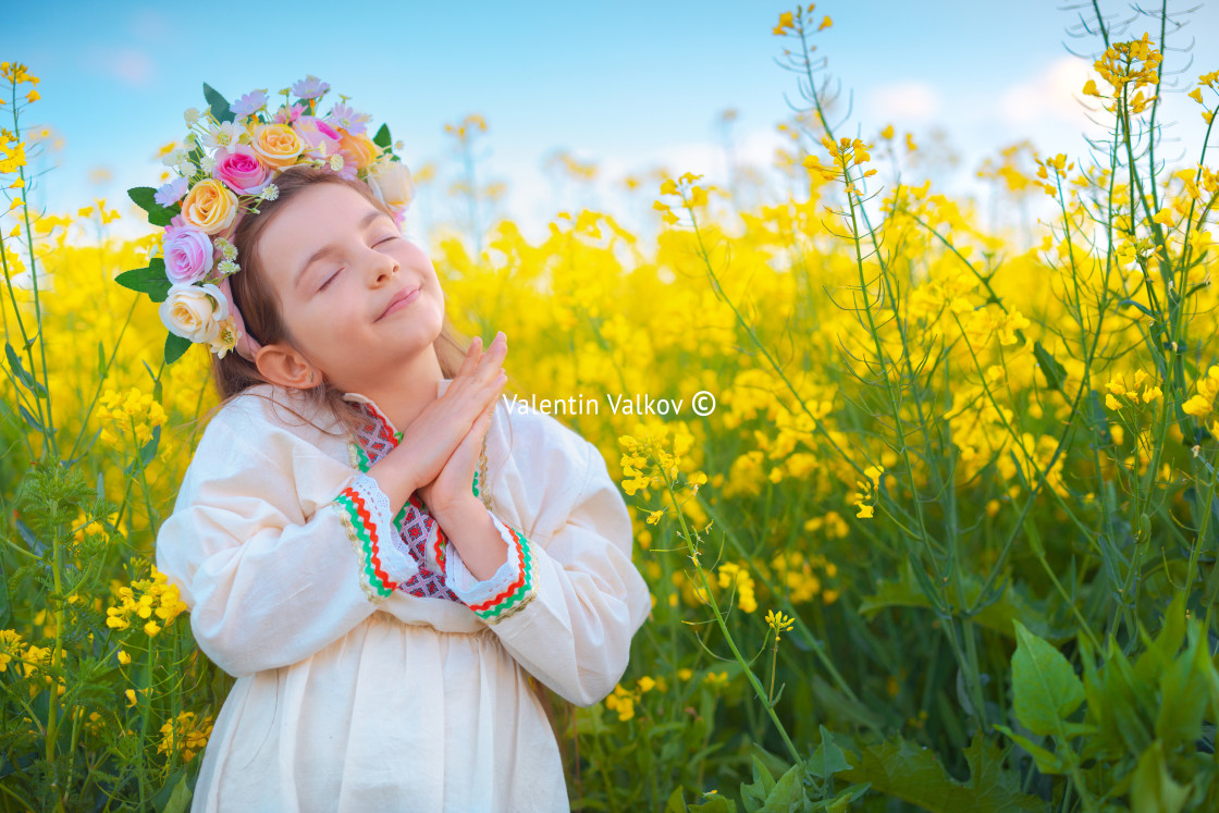 "Dreaming Beautiful young girl with flower chaplet, ethnic folklore dress with traditional Bulgarian embroidery during sunset on a rapseed agricultural field" stock image