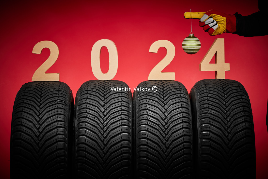 "Winter car tires, big wheels service and hand of mechanic man with wrench and christmas ball on red background." stock image