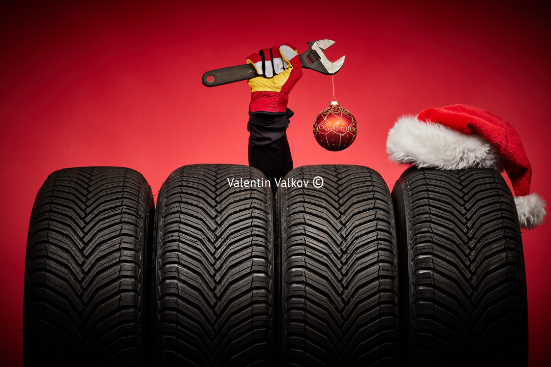 "Winter car tires, big wheels, tyres, mechanic hand with wrench, christmas tree ball and Santa Claus hat on red background" stock image