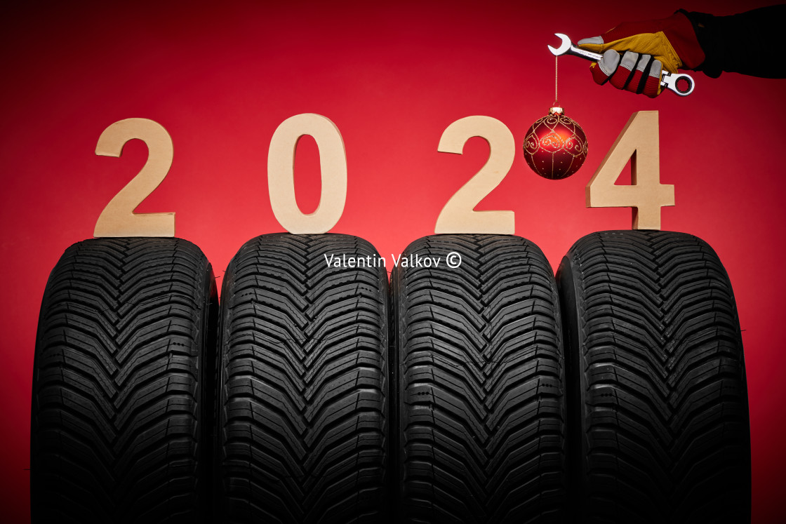 "Winter car tires service and hand of mechanic with wrench and christmas ball, text 2024 happy new year on red background." stock image