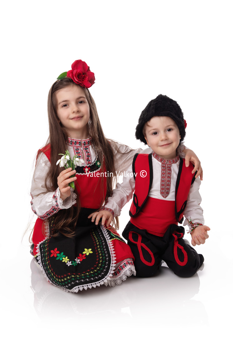 "Bulgarian kids boy and girl in traditional folklore costumes with spring flowers snowdrop and handcraft wool bracelet martenitsa symbol of Baba Marta" stock image