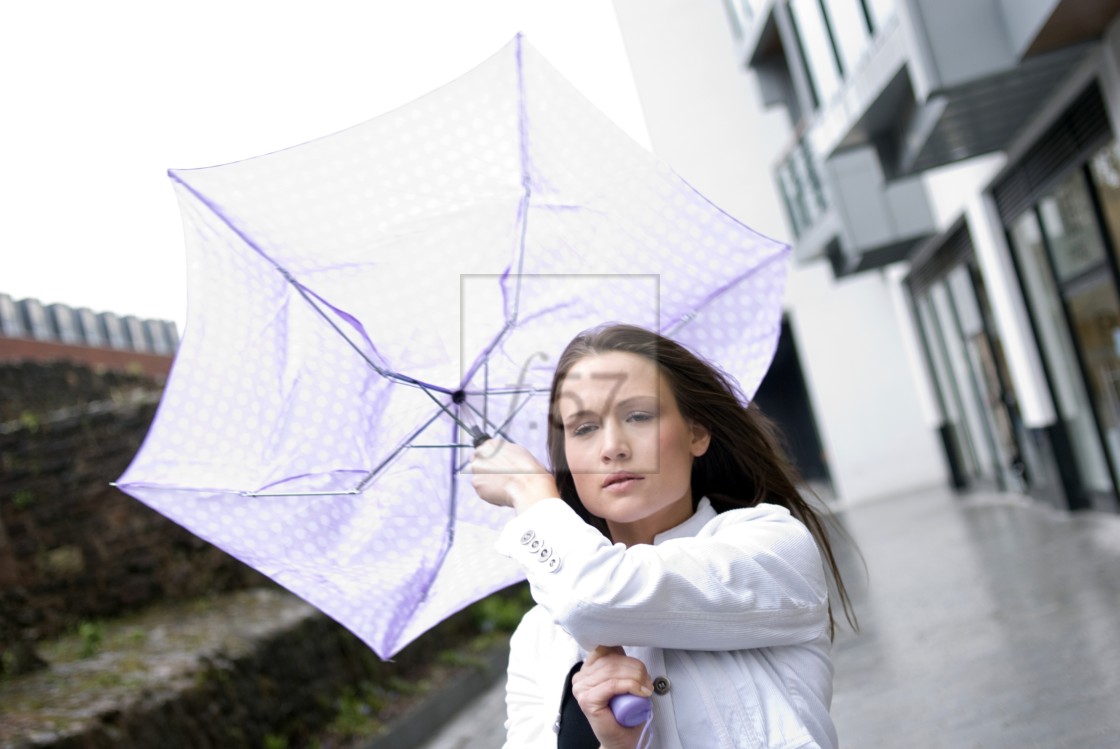 "Attractive young woman struggling as her umbrella is blown around in the wind on a rainy day." stock image