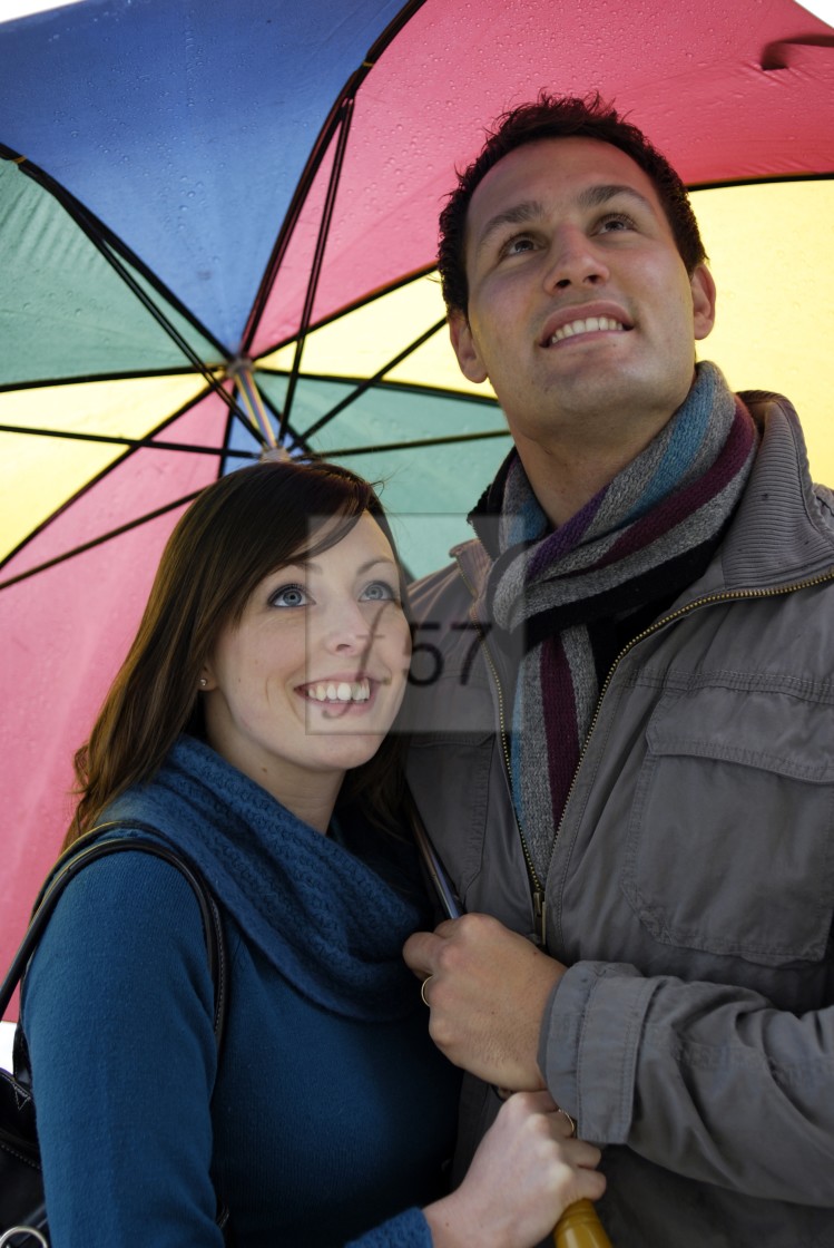 "A happy young couple looking up at the sky from under the shelter of a large colourful umbrella." stock image