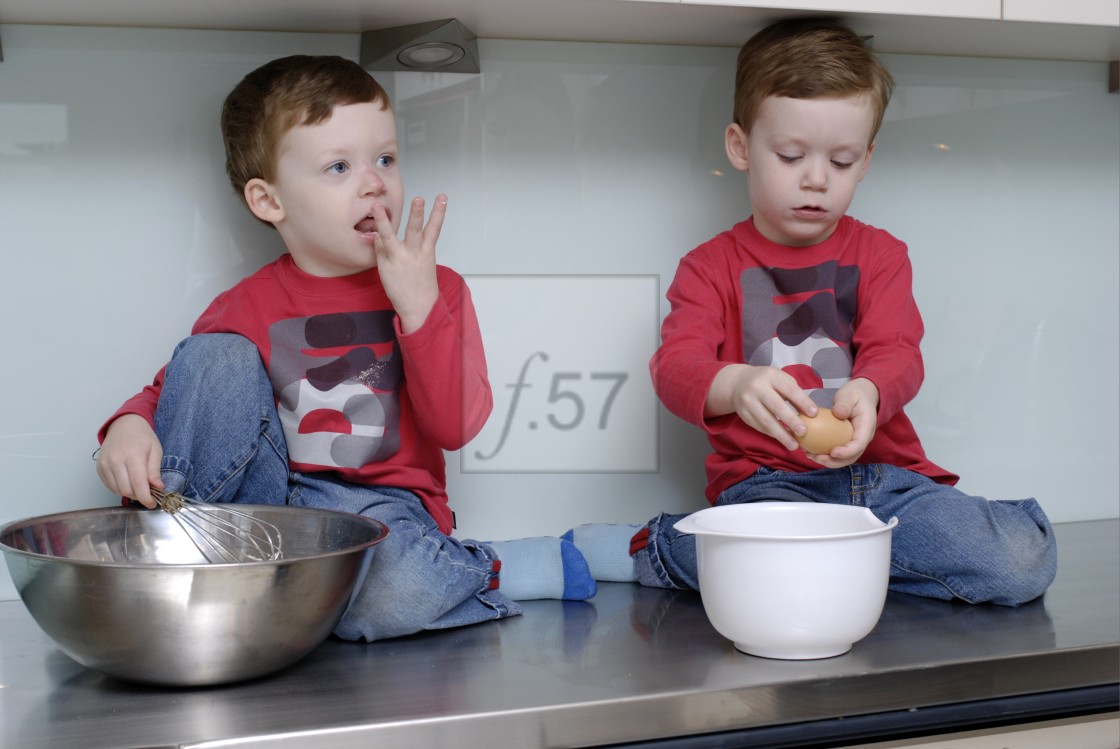 "Twin boys, three and a half years old, sitting on kitchen bench top to do some baking." stock image