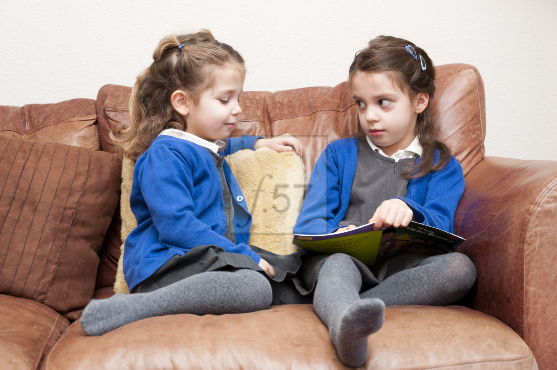 "Young sisters in Primary School uniform reading a book together." stock image