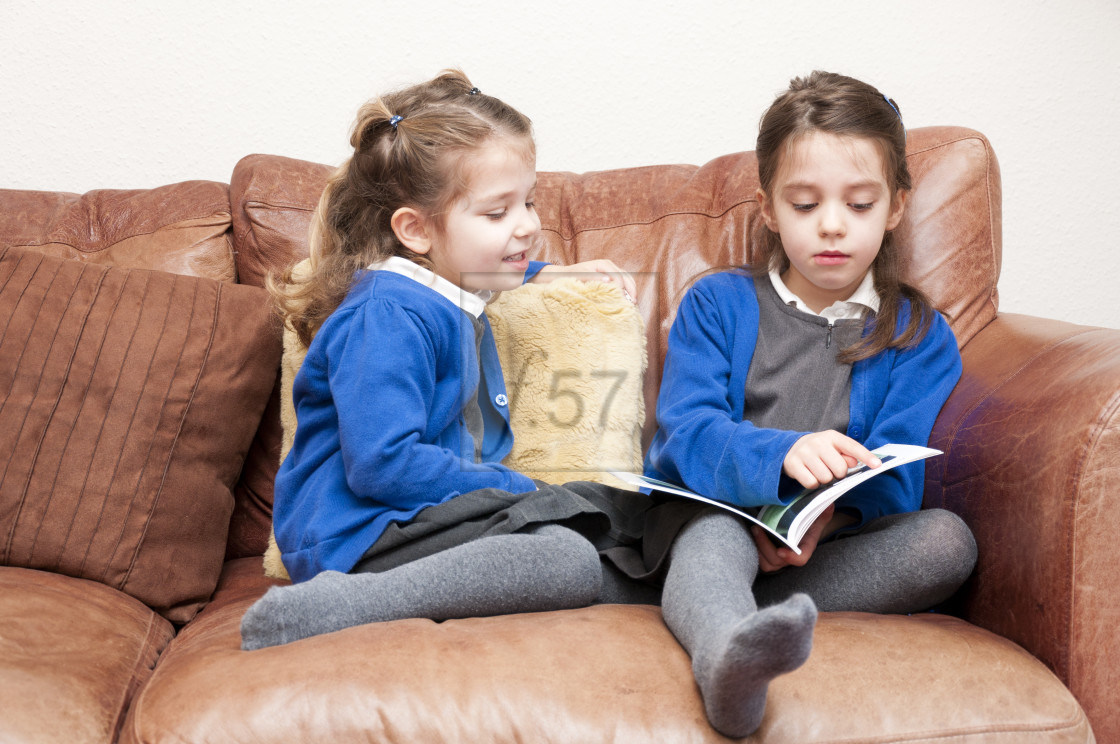 "Young sisters in Primary School uniform reading a book together." stock image