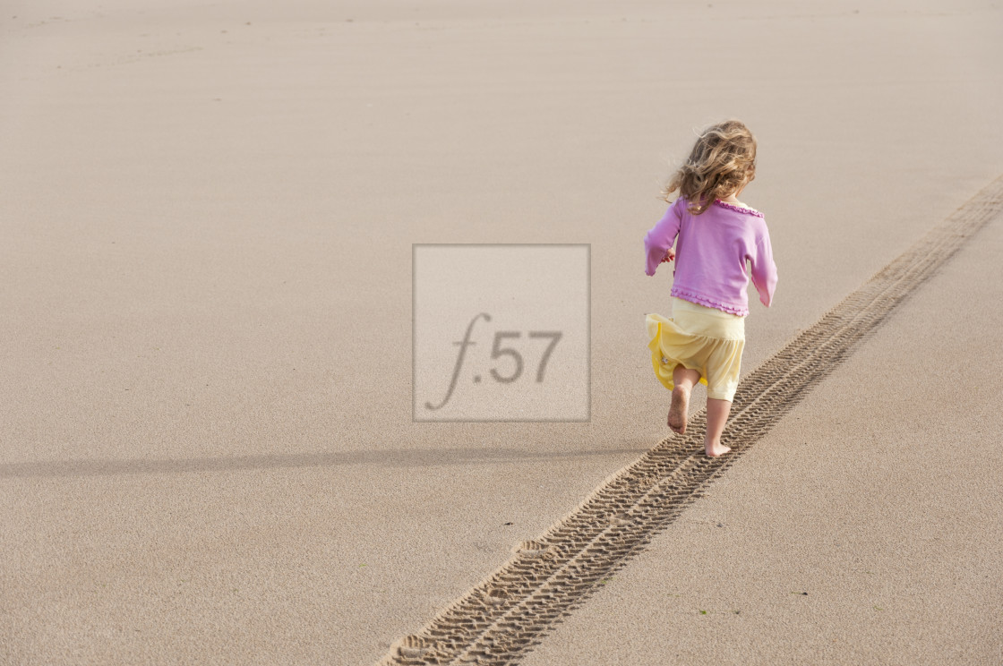 "Young girl, four years old, running along a tyre track on a sandy beach." stock image