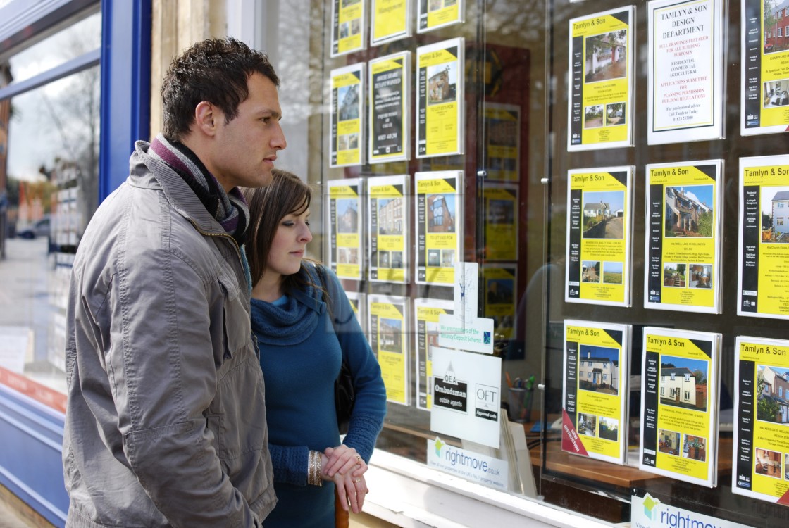 "Couple looking at property adverts in estate agent window" stock image