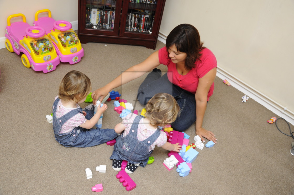 "Mum sitting on floor playing with young children" stock image