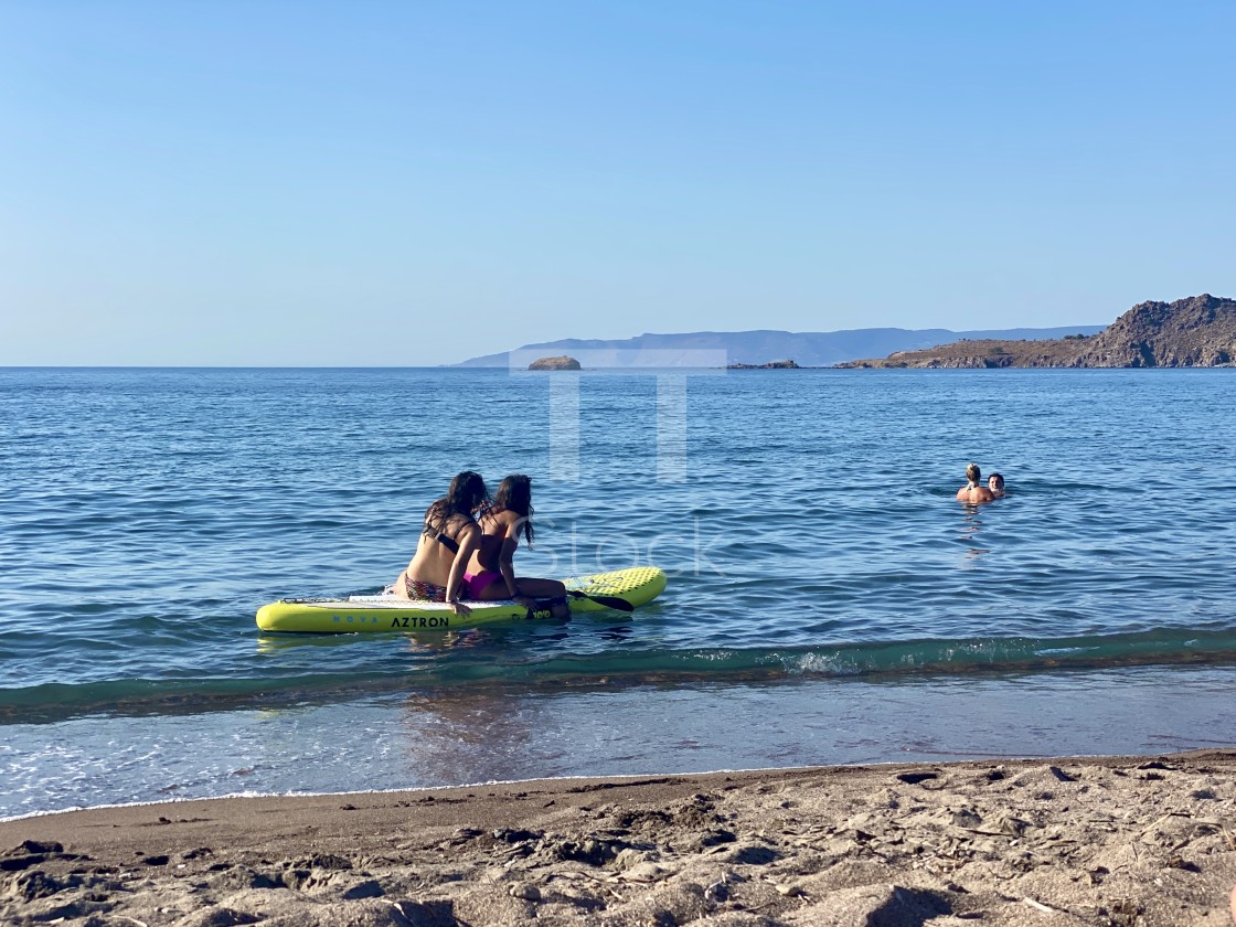 "Two young women friends at sea wearing bikini sitting and relaxing on a sup board by the beach." by TTStock - $7.54 "Two young women friends at sea wearing bikini sitting and relaxing on a sup board by the beach." stock image