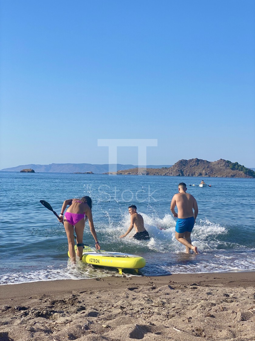 "Young woman wearing a pink bikini on the beach with a sup board, youths jump in the sea." by TTStock - $7.54 "Young woman wearing a pink bikini on the beach with a sup board, youths jump in the sea." stock image