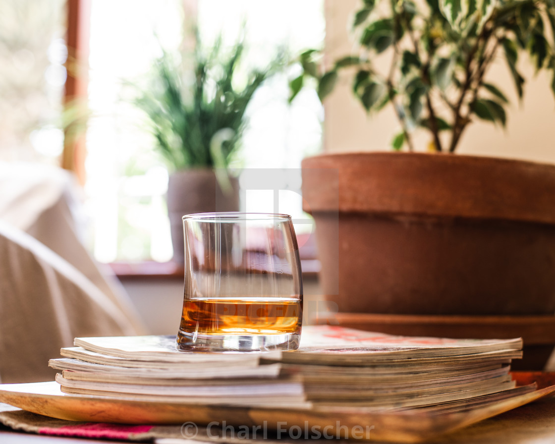 "A glass of whiskey sits on top of a pile of magazines in front of potplant and bright window" by Charl Folscher - £12.40 "A glass of whiskey sits on top of a pile of magazines in front of potplant and bright window" stock image