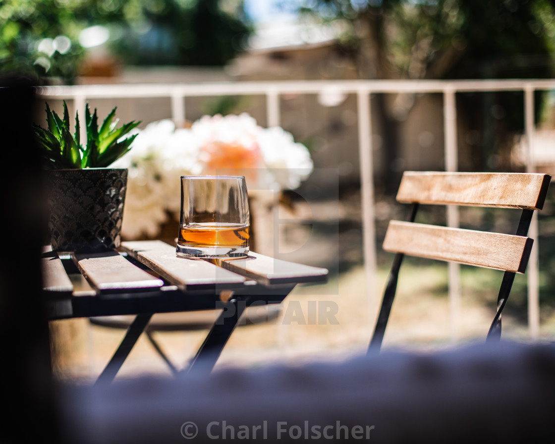 "A glass of whiskey on a small wooden table outside in the sun" by Charl Folscher - £12.40 "A glass of whiskey on a small wooden table outside in the sun" stock image