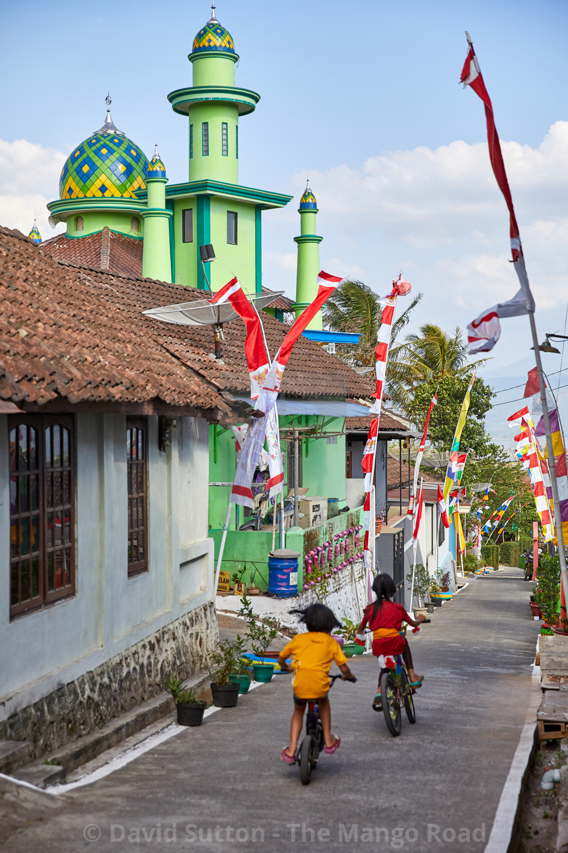 "Children ride bicycles past a mosque in a small kampung, or village in..." stock image