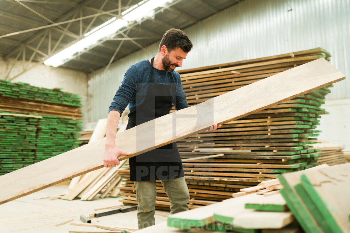 "Smiling man picking up a wood board in a workshop" by Foto Creativa - £3.80 "Smiling man picking up a wood board in a workshop" stock image
