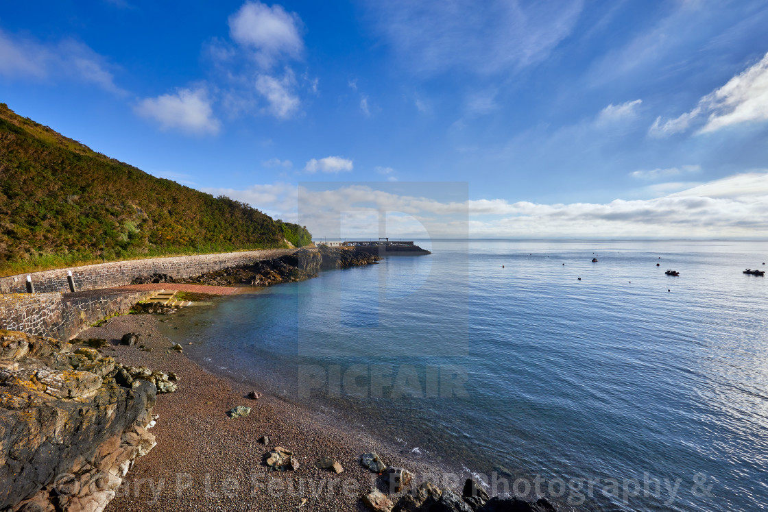 "Image of Bouley Bay on a sunny morning with blue sky with some cloud, pebble beach, smooth sea and harbour in the background. Jersey Channel Islands" stock image