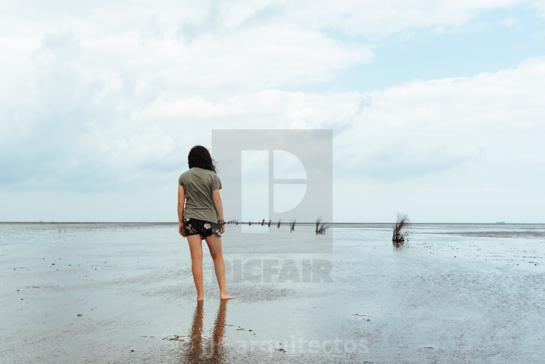 "Young woman standing alone in a calm and tranquil beach at low tide" stock image