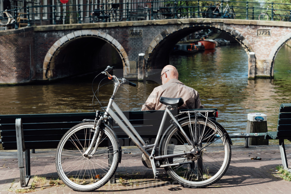 "Rear view of unidentified old man sitting at the waterfront of canal in Amsterdam" stock image