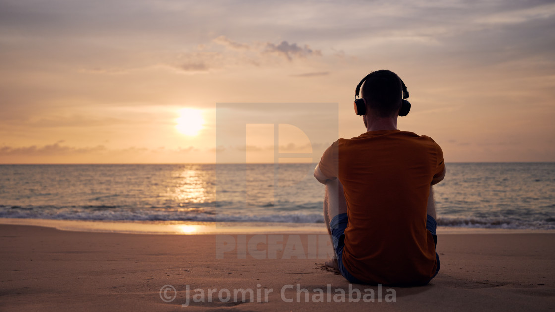 "Rear view of man with headphones on beach" stock image