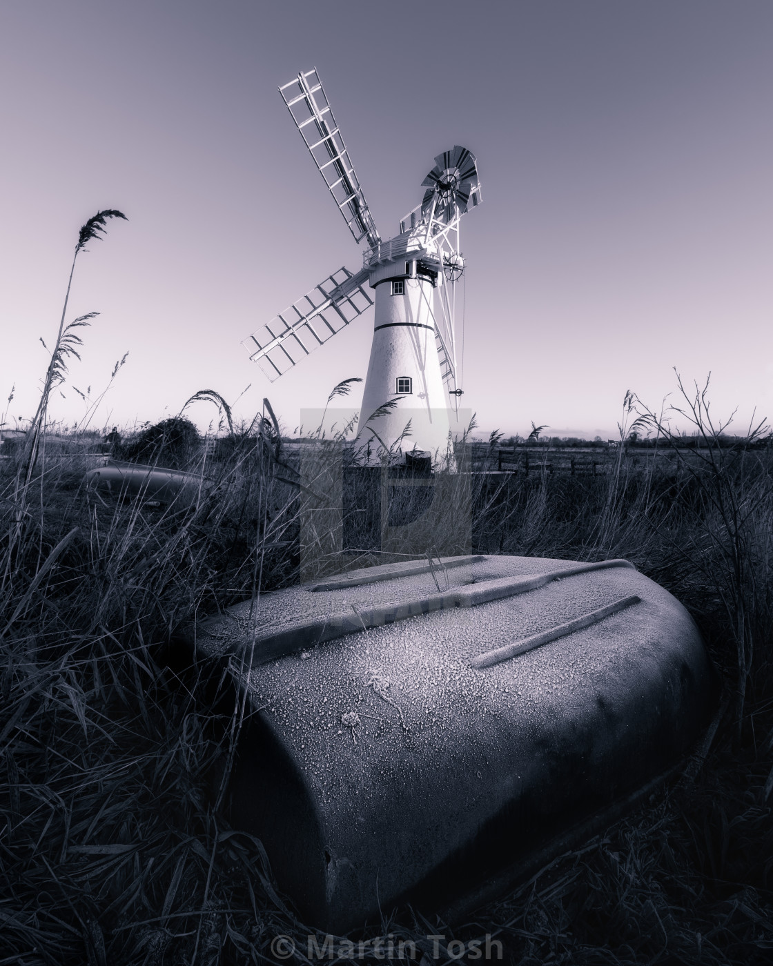 "Thurne windmill mono with upturned frost covered rowing boat." stock image