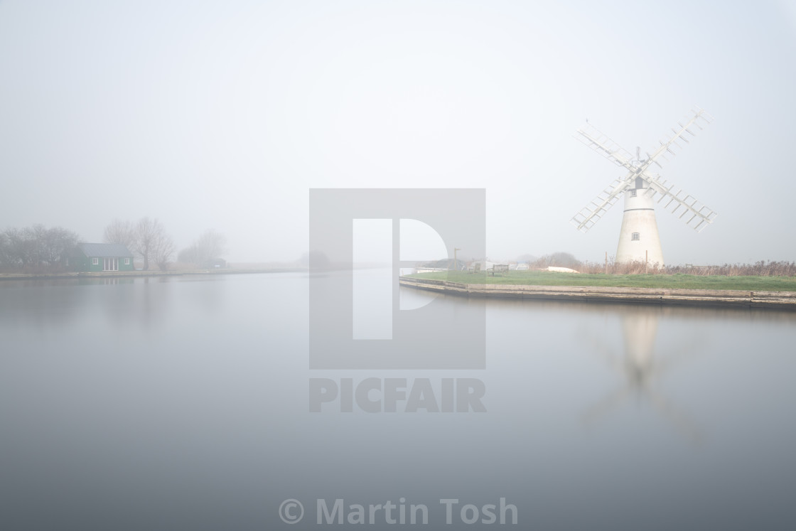 "Thurne mill across a long exposure of Thurne Staithe on a misty morning in the Norfolk Broads" stock image