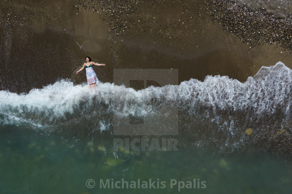 "Woman with white dress resting on a sandy beach with braking waves on the shore. Overhead shot. Aerial drone photograph" stock image