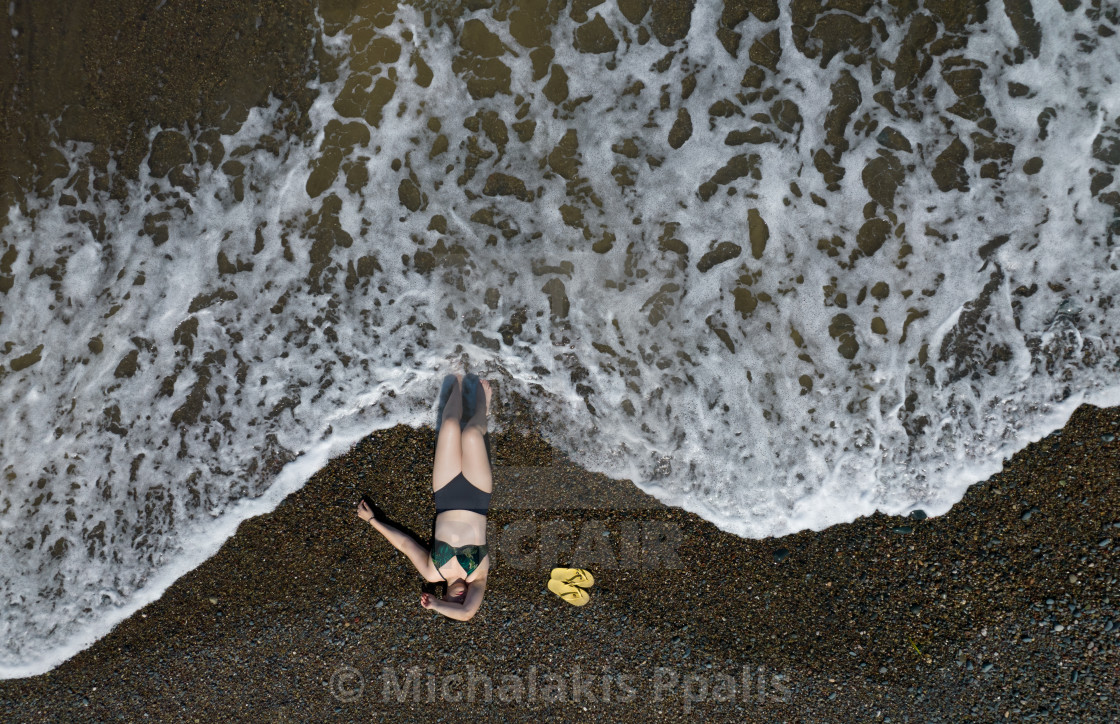 "Woman with swimsuit resting on a sandy beach with braking waves on the shore. Overhead shot. Aerial drone photograph" stock image