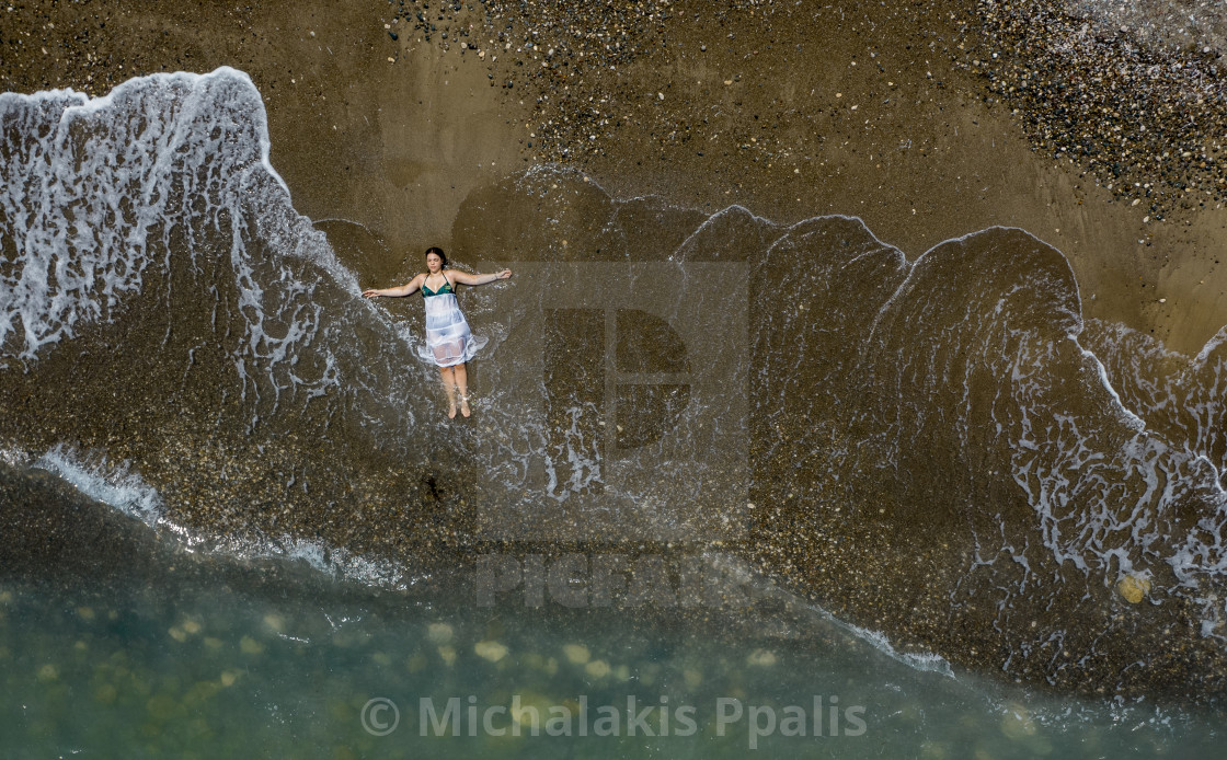 "Woman with white dress resting on a sandy beach with braking waves on the shore. Overhead shot. Aerial drone photograph" stock image