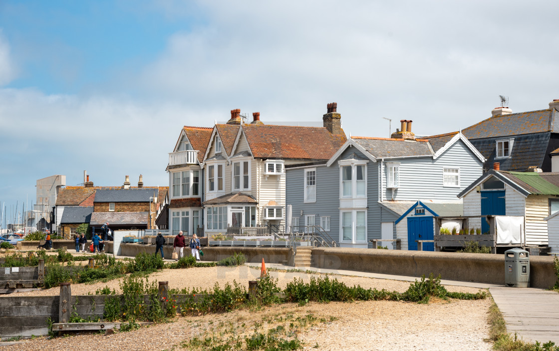 "Tourists and locals walk along the seafront pathway seaside with traditional British houses in Whitstable kent England." stock image