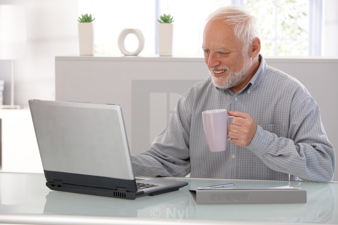 "Elderly man working on laptop smiling" stock image