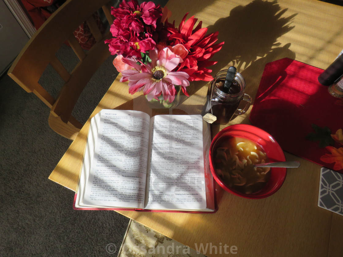 "open Bible book, soup, tea and flowers sitting on table in house for study in beautiful sunlight" stock image