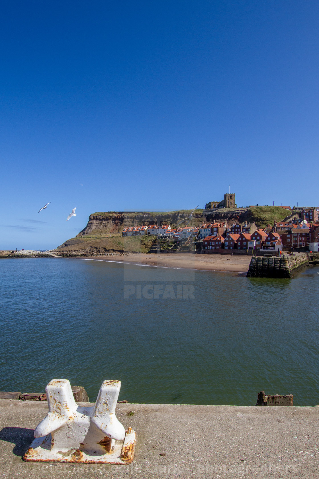 "Whitby,UK,Yorkshire,East coast, View across the Lower Harbour towards Tate Hill Pier and Sands. St Mary's Church in the background, ship Mooring Bollard in the Foreground. Photograph taken on a sunny day, April 2013" stock image