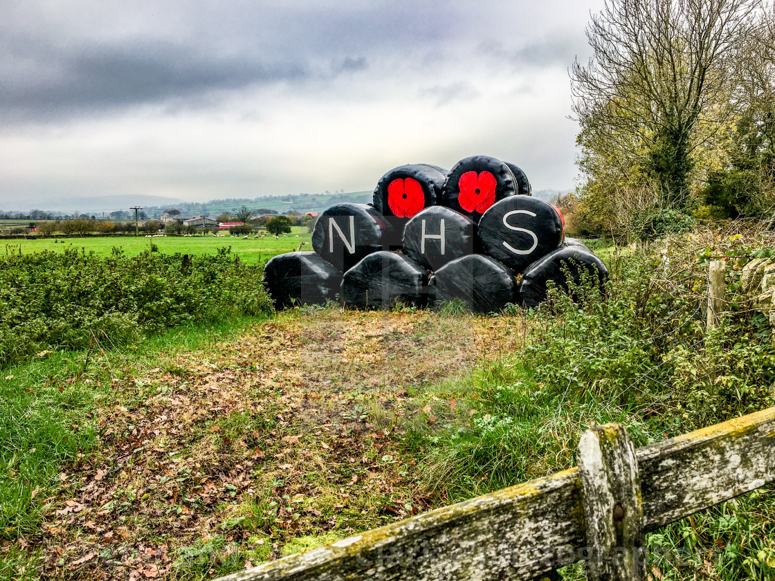 "Poppy Motif and NHS Logo on Plastic Covered Hay Bales. Fence to Foreground." stock image