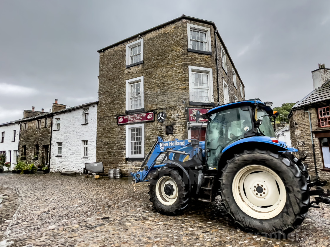 "Dent, Tractor travelling over cobbled street, Dentdale." stock image