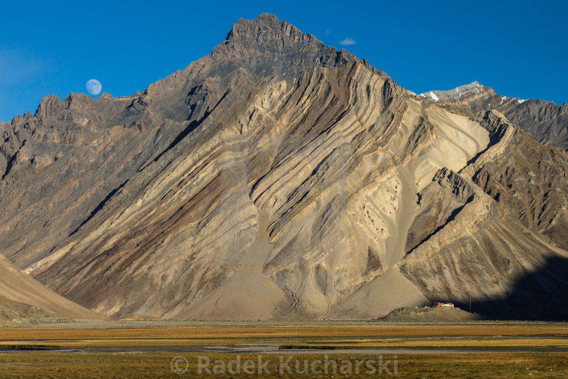 "Zanskar Mountains cliff with clearly visible sediment rock layers, Rangdum Gompa and the rising moon" stock image