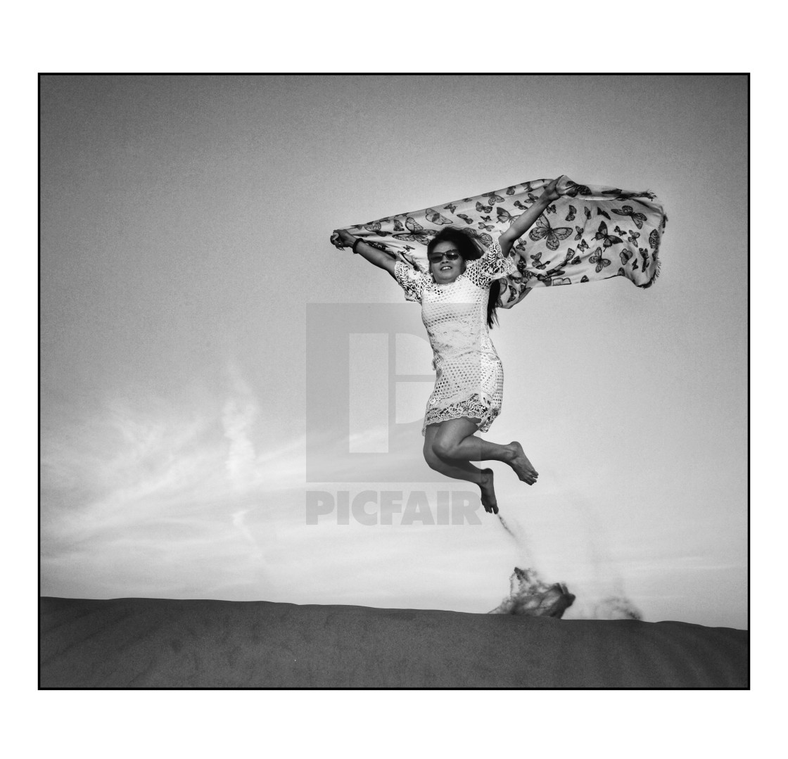 "Woman jumping in the sand with a scarf, mono" stock image