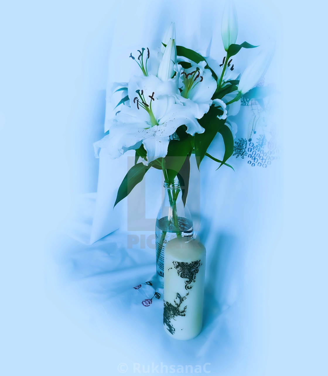 "White Lily flowers in. a glass bottle and a white candel" stock image