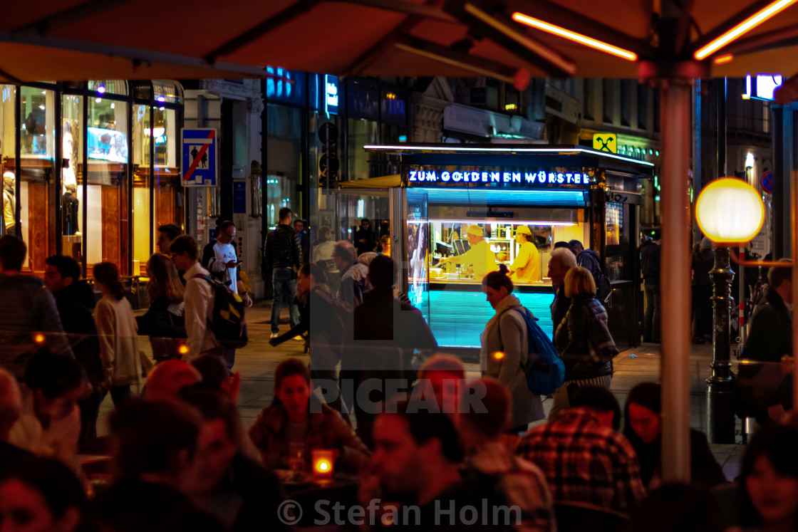 "Sausage stand in colorful neon lights on a busy street and guest" stock image