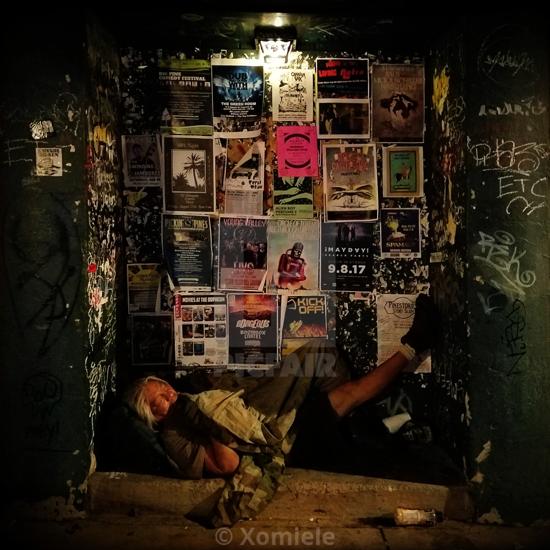 "A homeless man sleeps on the streets in an alcove amidst band flyers and graffiti." by Xomiele - $6.23 "A homeless man sleeps on the streets in an alcove amidst band flyers and graffiti." stock image